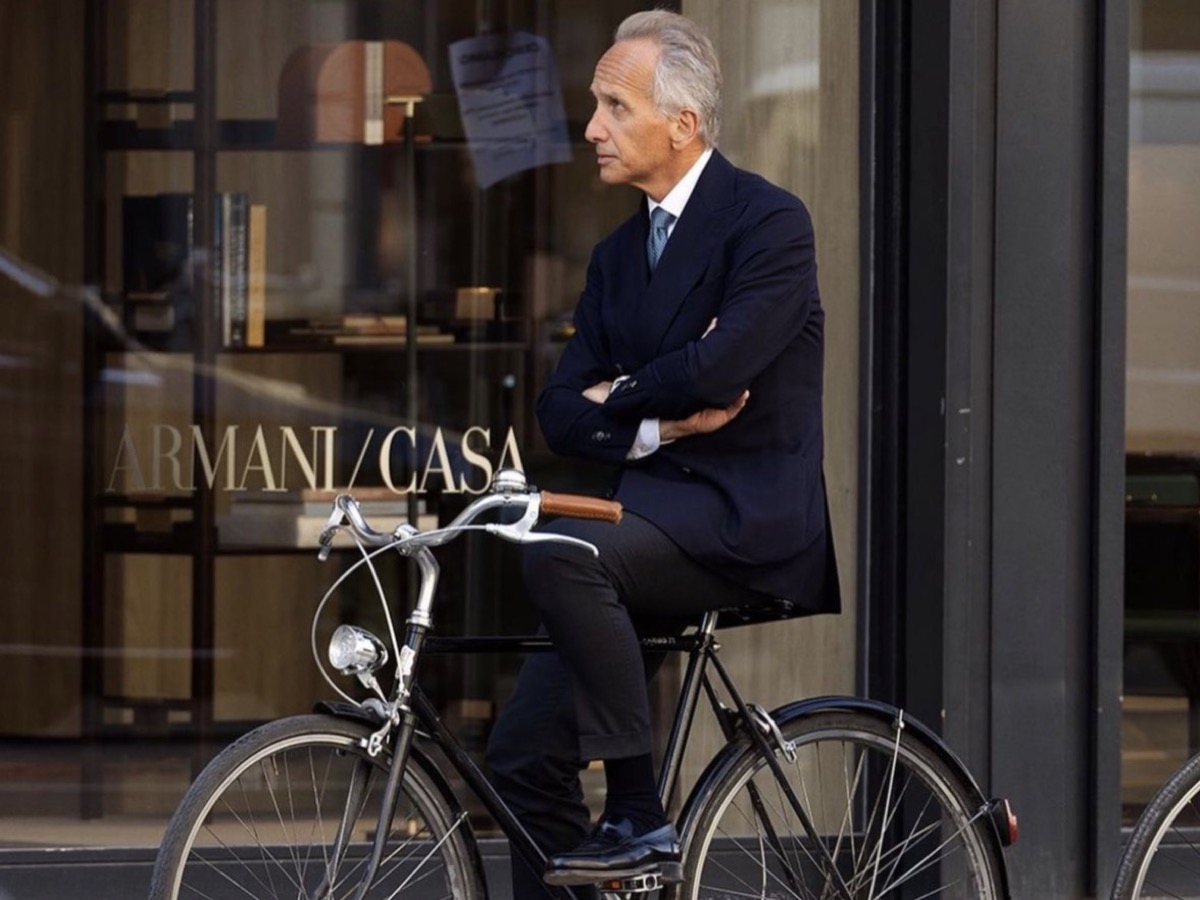 Executive man in navy tailoring seated on a city bicycle outside a refined storefront