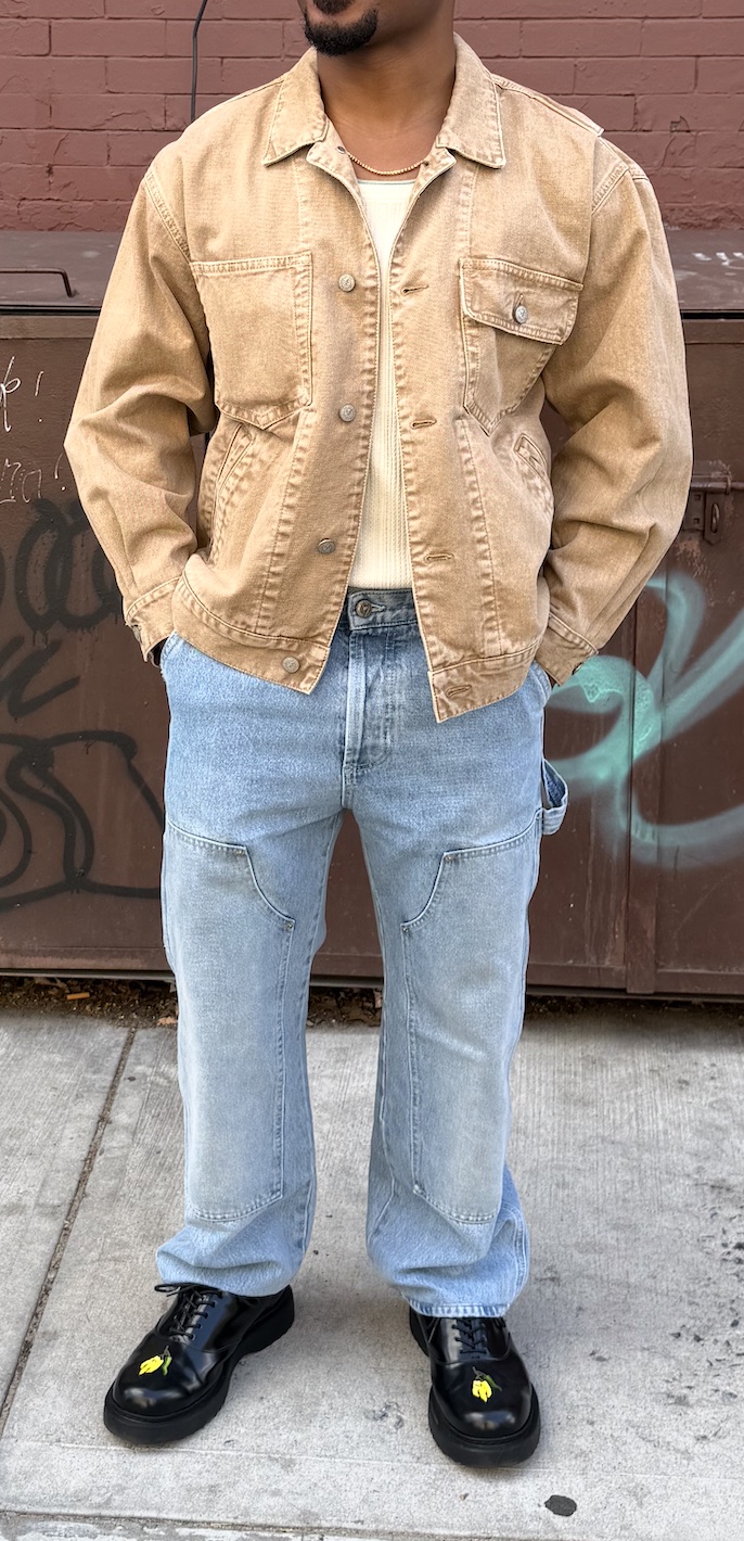 Colby L. wearing a tan jacket, cream knit top, light blue jeans, and black loafers