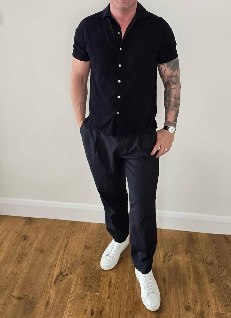 David O. wearing a black short-sleeve shirt, dark trousers, and white sneakers