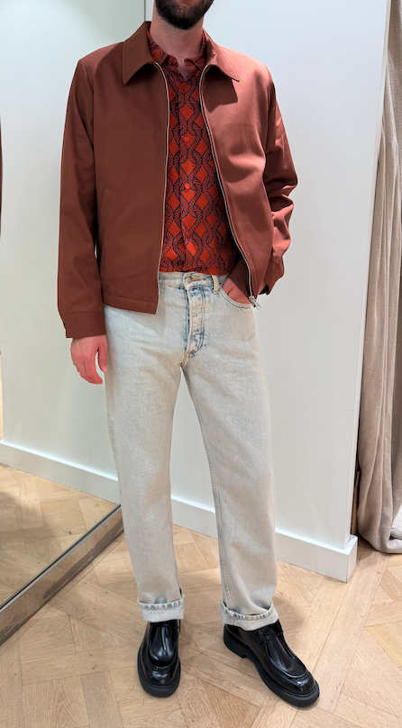 Jonathan L. wearing a rust jacket, patterned shirt, light jeans, and black loafers