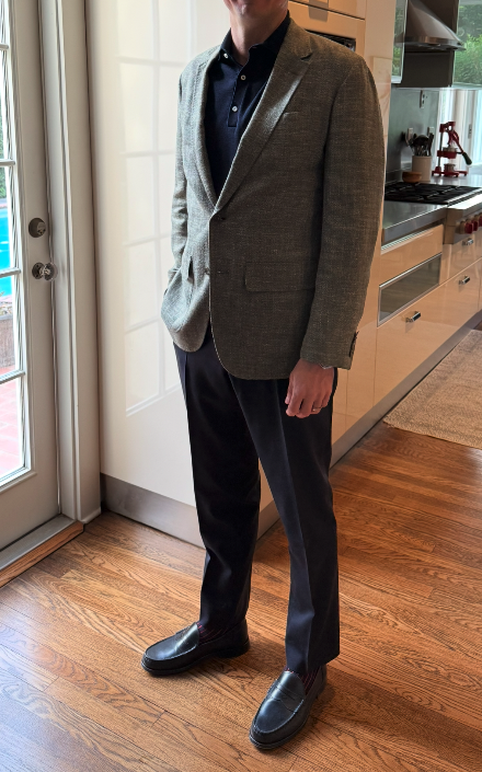 Ryan J. wearing a grey blazer, navy polo, dark trousers, and black loafers